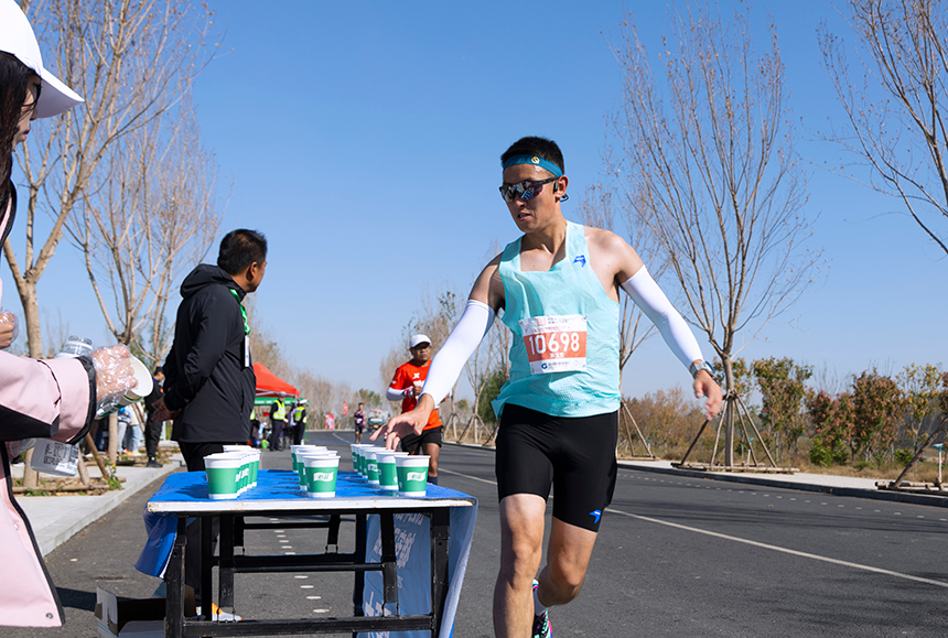 2023雄安馬拉松現(xiàn)場補給點參賽跑者正準備補給。齊鑫攝