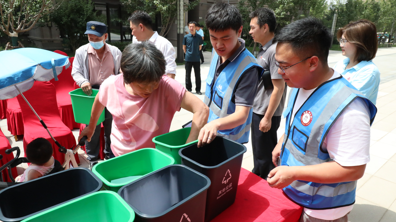 “垃圾分類志愿服務隊”隊員向居民發放垃圾桶。生態建設公司供圖